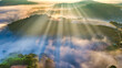 © huythoai - A breathtaking sunrise over mist-covered mountains, where golden sun rays stream through layers of fog and illuminate rolling green hills. In the foreground, terraced farmland and greenhouse structure