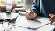 © Lek - close-up shot, businessman work on desk at home with documents checking business contract, working and meeting online via laptop and mobile phone