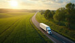 © miss irine - White semi truck drives on asphalt road through green fields. Sunny sky with clouds above the landscape. Trees line the country road. Nature scenery.
