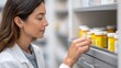 © snezhkina - Pharmacist in white coat carefully selecting medication bottles from a shelf