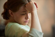 © DragonImages - Close up of young adult Caucasian female caregiver resting head on hand, showing stress and fatigue in nursing home
