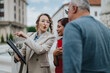 © qunica.com - Businesswoman explains plans to two clients while holding a clipboard outdoors. She gestures toward a nearby building as the clients listen attentively.