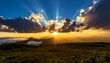 © davidolgade - Radiant sun bursts through clouds over a hilly landscape at dawn, creating a dramatic and scenic vista with light