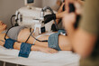 © qunica.com - Woman lying on treatment bed receiving a noninvasive body sculpting procedure on her abdomen. The aesthetic technician operates a fat-reduction device during a beauty center session.