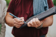© qunica.com - A man writes business notes in a black spiral notebook with a blue pen. Close-up shows his hands holding the notebook during an informal outdoor meeting.