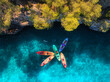 © den-belitsky - Aerial drone view of colorful kayaks with people in crystal clear turquoise sea near rocky coast and green trees. Summer outdoor adventure in Mallorca, Balearic Islands, Spain. Top down view of canoes