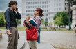 © qunica.com - Two business colleagues stand outdoors in conversation, one speaking on a mobile phone while the other holds folders and a red bag.