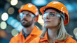 © MdAl - A professional industrial photograph of two workers in bright orange safety gear against a blurred background with bokeh lighting effects