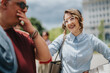 © qunica.com - A professional woman in glasses smiles while talking to a colleague outdoors. Casual business conversation between coworkers on an urban street.