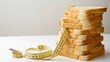 © nunoi - Stack of whole wheat bread slices with a yellow measuring tape wrapped around, symbolizing diet, portion control, and healthy eating.