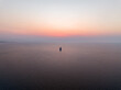 © AmazingAerialAgency - Aerial view of a lone sailboat sailing across the calm Mediterranean Sea under a soft sunset sky off the coast of Isola delle Femmine, Sicily, Italy.
