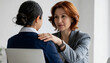 © budiawan - Mature businesswoman with red hair offers comfort and support to a younger colleague in a professional office setting, showing empathy and mentorship.