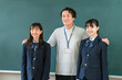 © buritora - A male teacher and female elementary, middle, and high school students standing in front of the classroom blackboard.