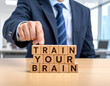 © magele-picture - Train your Brain - Geschäftsmann zeigt auf den Text 'Train your Brain'
