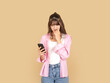 © Designerant - Worried young woman looking at smartphone and biting nail with anxious expression, reacting to problem or message concept idea. Isolated on beige background with copy space for advertising use.