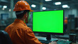 © Pete - Factory worker in orange uniform and hard hat sits at desk, looking at green screen computer monitor. Technician works on digital display in industrial setting, using keyboard and circuit board.