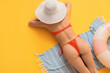 © Pixel-Shot - Beautiful young woman in stylish orange swimsuit with inflatable ring and beach blanket lying on yellow background, top view