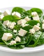 © Sarojah - Fresh spinach leaves on a white plate topped with cubed and crumbled white cheese. A healthy and simple lunch