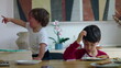 © Marco - Young children sitting at table during mealtime with one child crying and pointing while older sibling sits pensive and disengaged showing contrasting emotions in home environment
