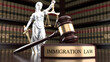 © Ali - A gavel and statue of justice on a desk in a law library with immigration law books