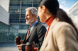 © Marko Geber - Smiling business colleagues walking with coffee outside modern office