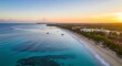 © brogar - Aerial view of a tropical coastline at sunrise with clear turquoise water, white sand beach, and resorts