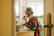 © Olga Moreira/Stocksy - Woman applying makeup with brush at bathroom sink