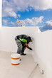 © Adrian Rodd/Stocksy - A painter, leaning over to paint the bottom part of a wall