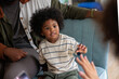 © Jovo Jovanovic/Stocksy - Young boy sits with family, reaching out with hand.