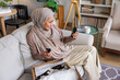 © Jovo Jovanovic/Stocksy - Woman in hijab unboxing beauty products at home.