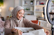 © Jovo Jovanovic/Stocksy - Woman in hijab smiles while unboxing a package.