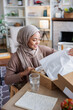 © Jovo Jovanovic/Stocksy - Woman in hijab smiles while opening a package.