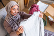 © Jovo Jovanovic/Stocksy - Woman in hijab smiles while unboxing new clothes.