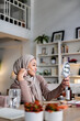 © Jovo Jovanovic/Stocksy - Woman in hijab applies makeup, smiling into hand mirror.