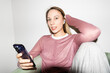 © Asya Molochkova/Stocksy - Woman with Phone and Headphones on Chair Against White Wall
