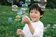 © zhang yongxin - A young child smiling and reaching for floating soap bubbles in a grassy outdoor setting