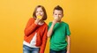 © Jane - children enjoying citrus fruits together, girl in orange cardigan and boy in green t‑shirt laughing playfully against bright yellow studio background