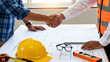 © NaesyaStudio - Construction professionals shaking hands over blueprints, symbolizing a successful agreement and collaboration in a project