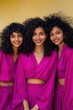 © Iryna - Three asian young female friends in matching magenta outfits smiling vertical portrait curly hair yellow backdrop youthful elegance