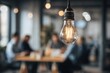 © salam - A close-up of a lit lightbulb hanging in front of an out-of-focus group of people
