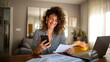 © Taras Vykhopen - Woman sits at home table checking bills on smartphone while smiling during daytime