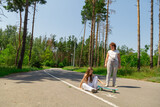 Active happy grandmother and granddaughters having fun time together skateboard in the forest.
