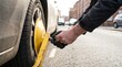 © Stitch - Parking enforcement officer hands locking a yellow wheel clamp onto a car tire on a city street