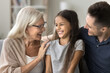 © fizkes - Multi-generational family enjoy time together, talking, laughing, resting on sofa at home. Cute little girl spend pleasant weekend leisure with loving granny and daddy. Ties, bonding, three generation
