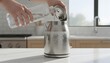 © antuanetto - A person descaling a stainless steel electric kettle in a bright modern kitchen for home maintenance concept with fresh water pouring from a glass bottle