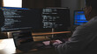 © onephoto - programmer working at a multi monitor computer setup with code on screens in a dark workspace, illustrating software development, coding, debugging, and technical workflow in office context.