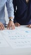 © rogerphoto - Business colleagues are examining financial data, pointing at charts and graphs spread out on a table during a collaborative analysis session in a modern office.