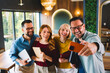 © djile - Diverse team of colleagues smiling and taking a selfie together in a stylish restaurant during a casual meeting