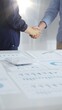 © rogerphoto - Businesspeople shaking hands over a conference table, finalizing a deal with financial documents and digital tools. Handshake concept