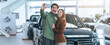 © Prostock-studio - A couple stands close together in a car dealership. They smile and take a selfie. The background shows several cars for sale and bright lighting from large windows.